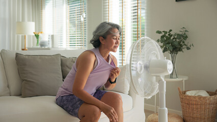 Asia adult people middle age old woman sit at sofa home feel hot flash fever use fan waving hand...
