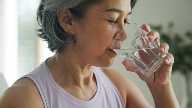 Asia adult people middle age happy old woman smile look at camera drink water stay hydrated reduce hot flash dry skin health care sit at home sofa elder aging asian aged female. Medical food relief.