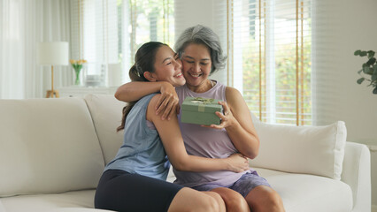 May Mother's day young adult child arm around cuddle hug give gift box to mature middle age old...