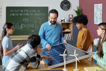 Teacher showing students principles of renewable energy using solar panels and wind turbine models...