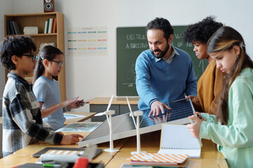 Teacher explaining function of solar panel to diverse group of students during science class, fostering curiosity and engagement with hands-on learning