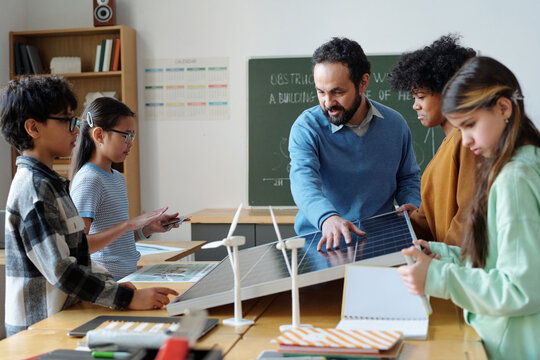 Teacher explaining function of solar panel to diverse group of students during science class, fostering curiosity and engagement with hands-on learning