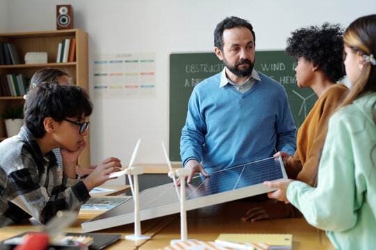 Students and teacher engaged in discussing renewable energy projects at classroom table displaying model wind turbines and solar panels, fostering collaborative learning - Powered by Adobe