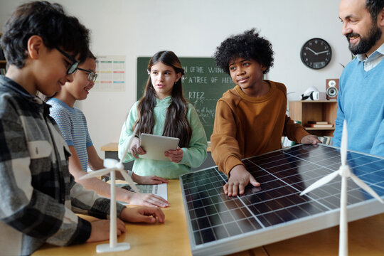 Group of students and teacher engaging in discussion about renewable energy project in classroom setting. Students and teacher examining solar panel model while holding various devices - Powered by Adobe