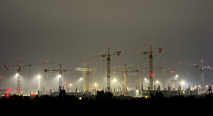 Construction Cranes at Night with Yellow and Red Lights Against Dark Sky Silhouette in City Landscape