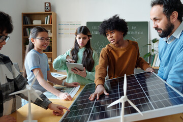 Students in classroom learning about renewable energy with solar panel and wind turbines. Involving...