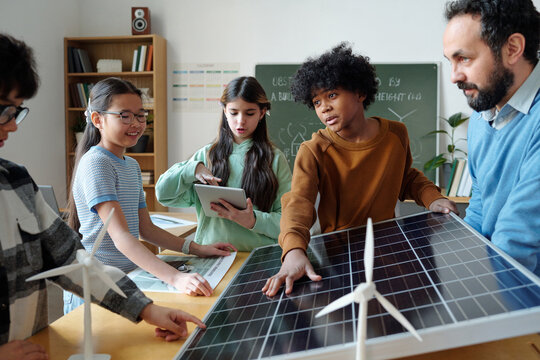 Students in classroom learning about renewable energy with solar panel and wind turbines. Involving diverse group of young learners with Caucasian and Hispanic teacher facilitating discussion
