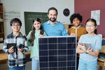 Group of students and teacher displaying large solar panel in classroom setting, highlighting renewable energy education and technology integration