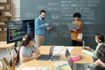 Teacher explaining properties of molecules using digital display while students engaging with...