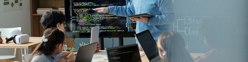 Teacher educating students on various programming languages in a classroom, with students actively participating and interacting with digital devices during lesson