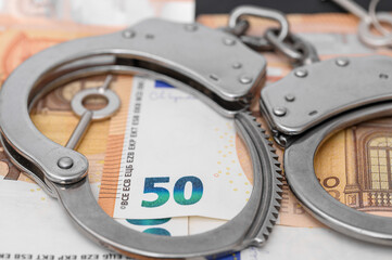 Banknoty euro i kajdanki, oszustwo finansowe, zlodziej