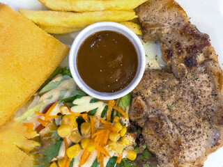 Grilled pork, fries, salad with corn, cornbread, and a cup of brown sauce.