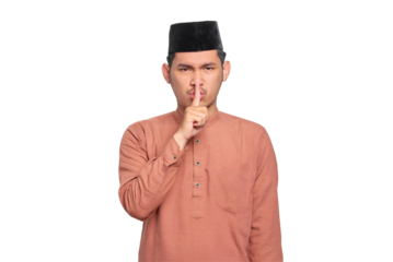 Serious young Asian Muslim man showing silence gesture with finger isolated on transparent background