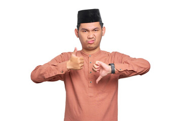 Serious young Asian Muslim man showing thumbs up and down decision isolated on transparent...