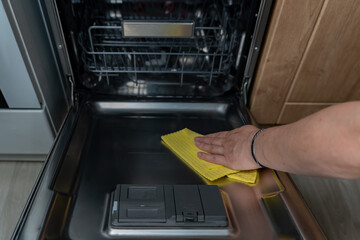 Woman's hand wipes the dishwasher with a yellow cloth. Eco-friendly dishwashing detergent. Maintaining cleanliness in the kitchen.