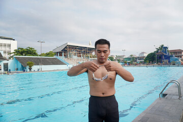 Shirtless Asian man preparing to swim, wearing goggles in public pool