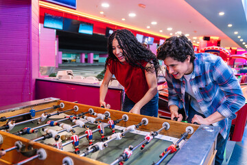 Two friends enjoying themselves while playing table football in a bowling alley with arcade games