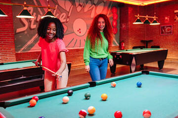 Fototapeta premium Two female friends enjoying a game of billiards in a vibrant bowling alley and arcade video game room