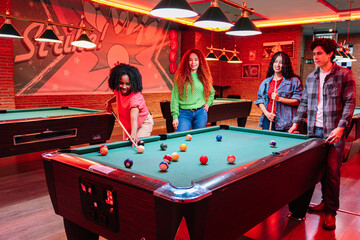 Group of young multicultural friends playing billiards in a bowling alley entertainment center, enjoying their leisure time together