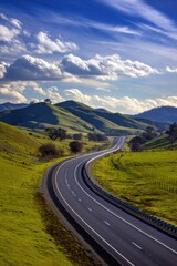 Naklejka premium Serene road winding through green hills under a bright blue sky with fluffy clouds rural landscape scenic route travel destination natural beauty peaceful journey