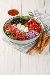 Pizza salad tosses mix of romaine lettuce, sausages, mozzarella, black olives and red onion in a fresh, grated tomato vinaigrette closeup on the plate on the wooden table. Vertical