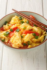 Soft silky eggs stir fried in a sweet tangy tomato sauce with green onions closeup on the plate on the wooden table. Vertical