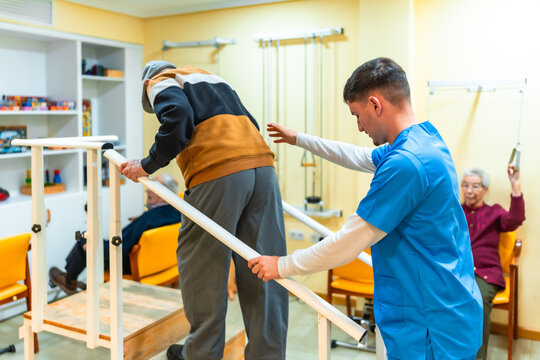 Nurse assisting elderly man using parallel bars in nursing home