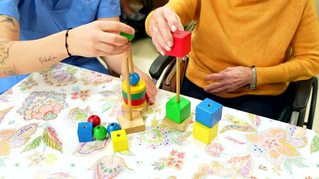 Nurse assisting elderly woman playing with building blocks