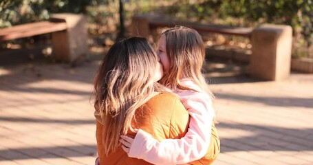 Tender moment between woman and young girl embracing on sidewalk. Mother kisses child standing close suggesting loving relationship on sunny day