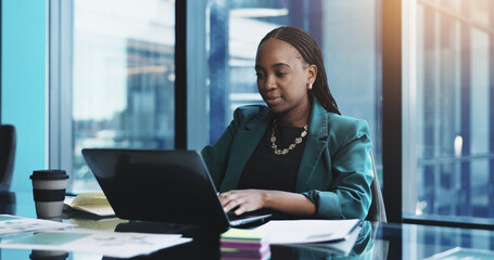 Fototapeta premium Black woman, laptop and typing with documents for business research, planning or design at office desk. Female person, computer and paperwork with internet for project, schedule or tasks at workplace