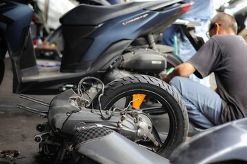 Mechanic inspects and repairs damage of their customers' motorcycles at bengkel motor.