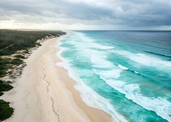 Aerial view of ocean waves crashing on a sandy beach. Turquoise water meets pale sand
