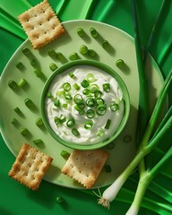 A plate of creamy sour cream with thinly sliced ​​green onions, surrounded by rustic square crackers on a bright green background.