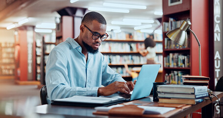 University, books and man in library on laptop for online research, information and studying for project. College, student and person with computer and notes for education, knowledge and learning