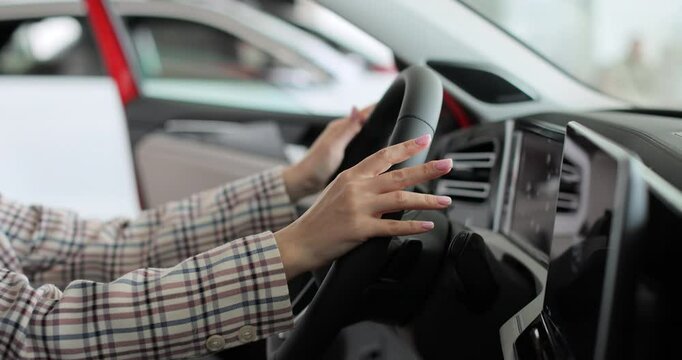 Close up hands young woman auto driver car owner holding steering wheel buy new automobile dealership inside vehicle. Concept of car shopping, buying, and dealership.
