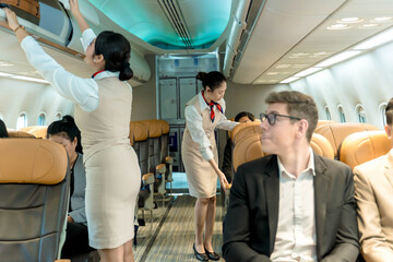 Cabin crew assists passengers by securing luggage in overhead bins and ensuring safety inside airplane cabin before departure on a commercial flight