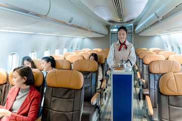 Flight attendant pushing food service cart in airplane aisle, providing in-flight meal and beverage service to passengers seated in economy class cabin