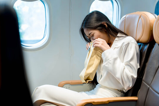 Young woman feeling air sickness on airplane, using vomit bag during flight, experiencing nausea and discomfort while seated in passenger cabin