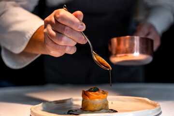  Chef en pleine préparation d’un plat gastronomique raffiné dans une cuisine de restaurant, illustrant précision culinaire et créativité.
