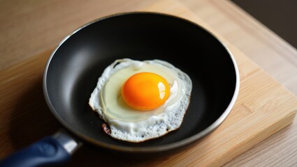 A fried egg in a black pan on a wooden cutting board.