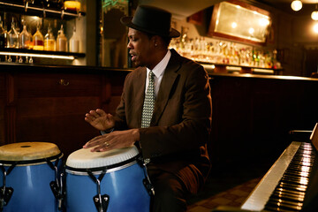 Medium shot of Black male musician in hat playing traditional conga drums, while performing Afro...