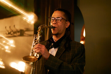 Medium shot of talented male musician with eyeglasses concentrated on playing melody on saxophone...