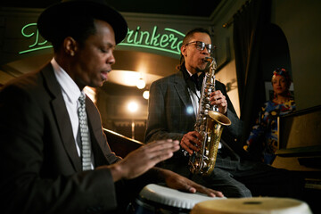 Medium full shot of multiracial male musician playing saxophone during jam session with jazz band while performing in bar