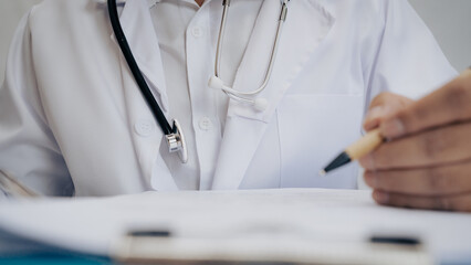 Close-up of doctor with stethoscope sitting and writing prescription at desk. Healthcare professional ready for consultation, diagnosis, and patient care.
