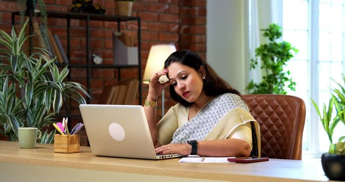 Suffering from headache neck pain while working on laptop, Indian young businesswoman in traditional ethnic saree sits stressed at cozy office desk under work pressure in modern corporate environment
