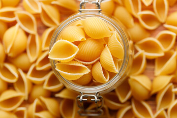 Raw uncooked dried Conchiglie shell pasta. Italian seashells pasta in lock lid jar on wooden background.