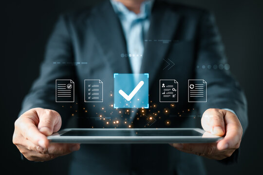 A business professional holds a tablet displaying floating document icons, a large checkmark symbolizing digital approve processes, focusing on business quality assurance and data management.