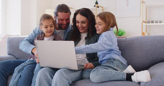 Happy young family at home with laptop online, parents, little kids on sofa in kitchen have fun using modern new computer together, enjoy weekend with small children, watch video, make order 
