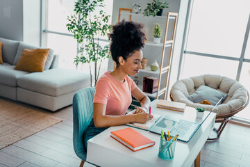 Young woman studying at home in a cozy living room with natural light, focused on learning and...