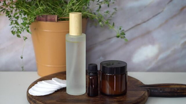 Natural homemade face toner in frosted glass bottle with essential oil and face cream in amber glass jar. Set on dark wood and marble background. Organic skincare and beauty concept.